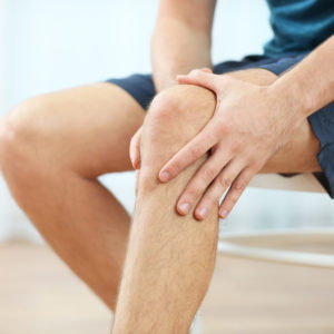 Young man suffering from knee pain at home, closeup